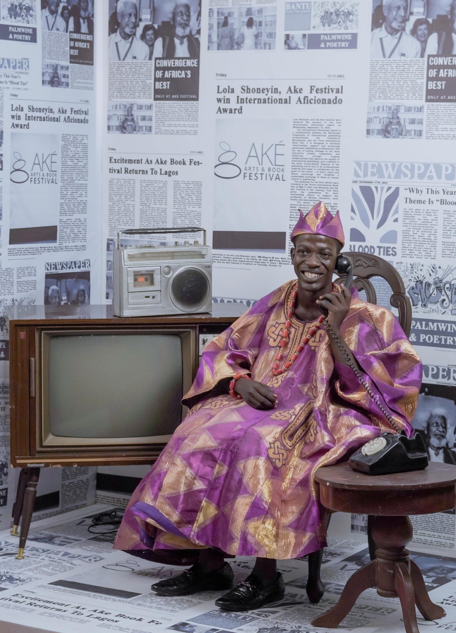 Aremo gemini sitting down beside a black and white old tv and putting an old land phone to his ears